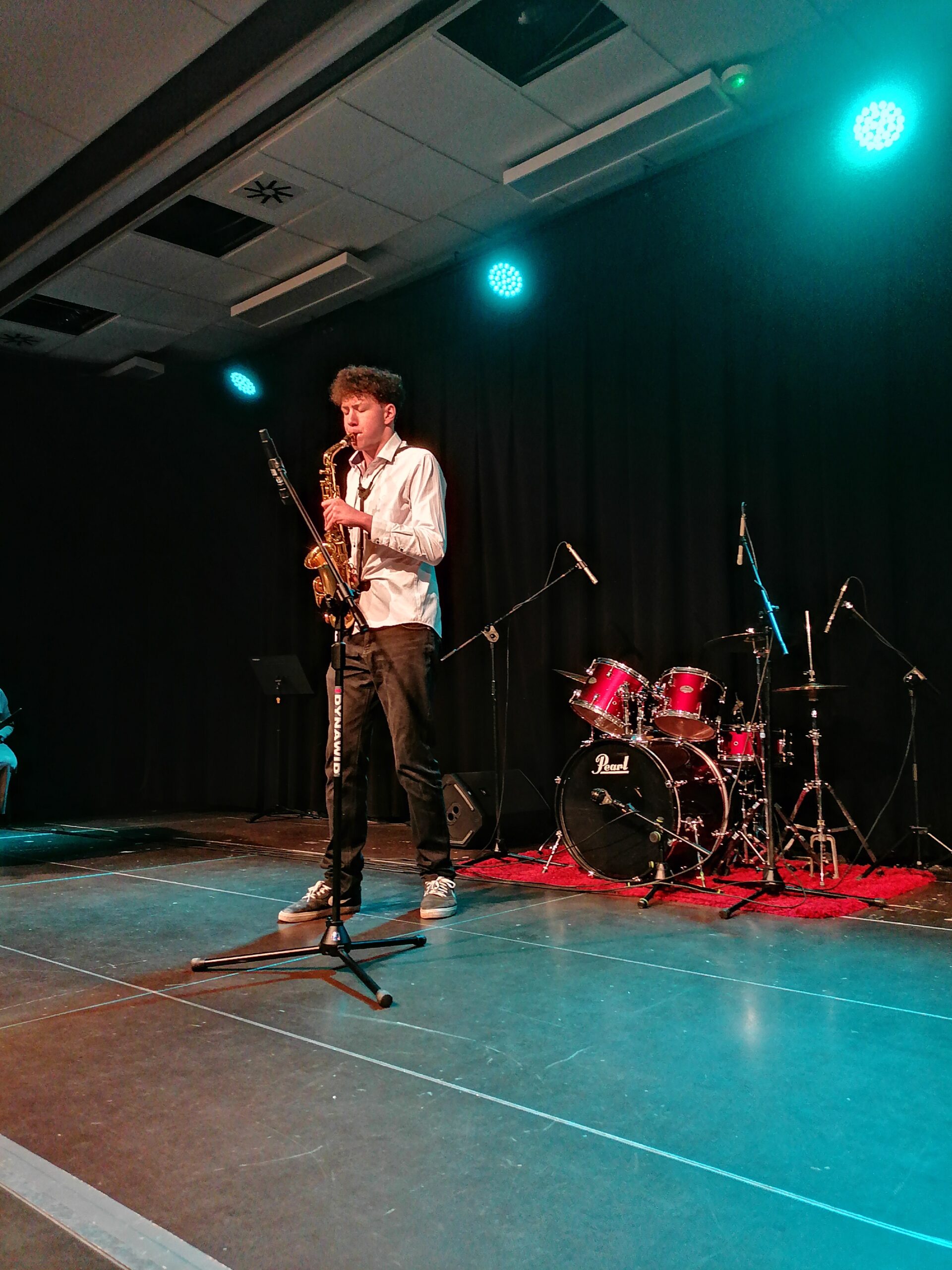 Uczeń grający na saksofonie podczas występu, w tle instrumenty perkusyjne